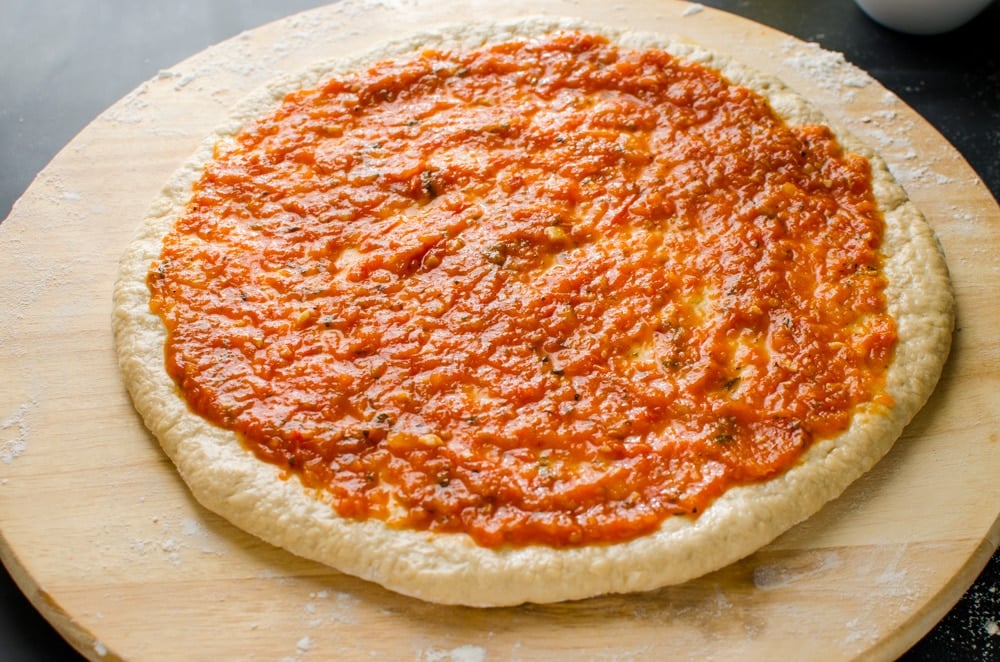 An image with a thin layer of fresh tomato pizza sauce over the rolled pizza base.