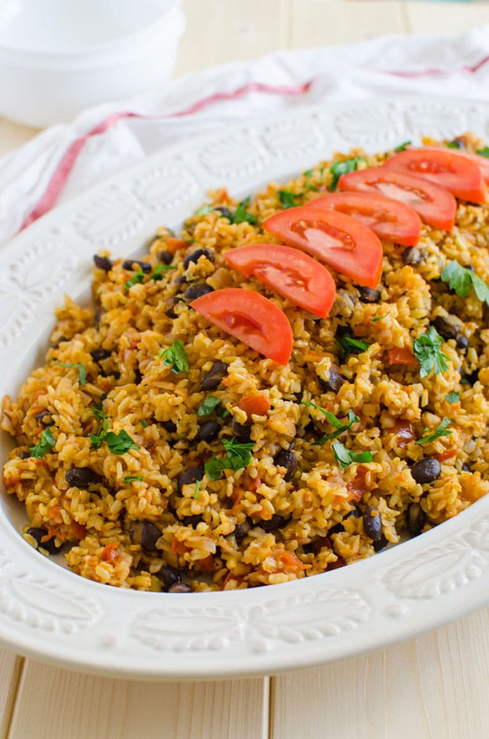 Mexican brown rice garnished with fresh tomato slices in a serving platter. 