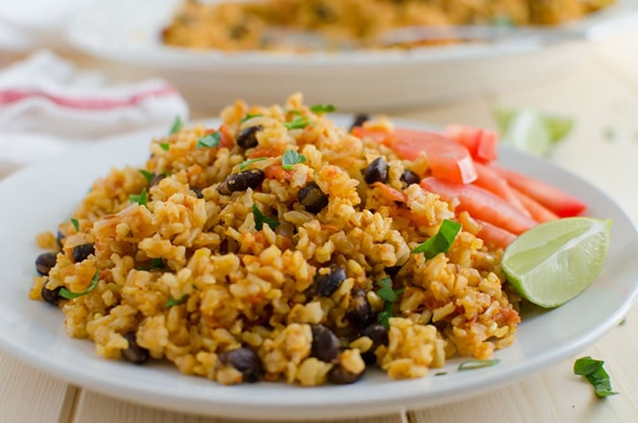 Mexican brown rice garnish with fresh tomato slices and a lime wedge in a serving dish. 