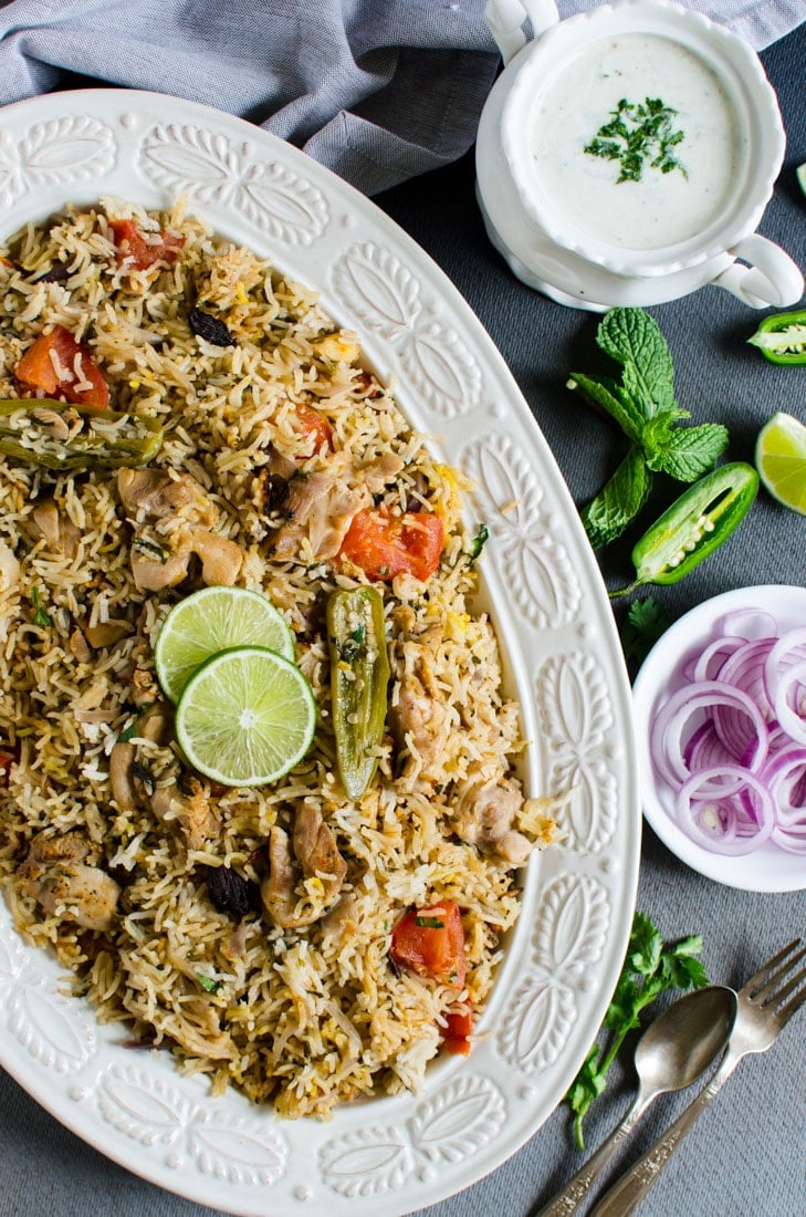Healthy chicken biryani rice in a large platter with sliced onion and yoghurt dipping on the side.