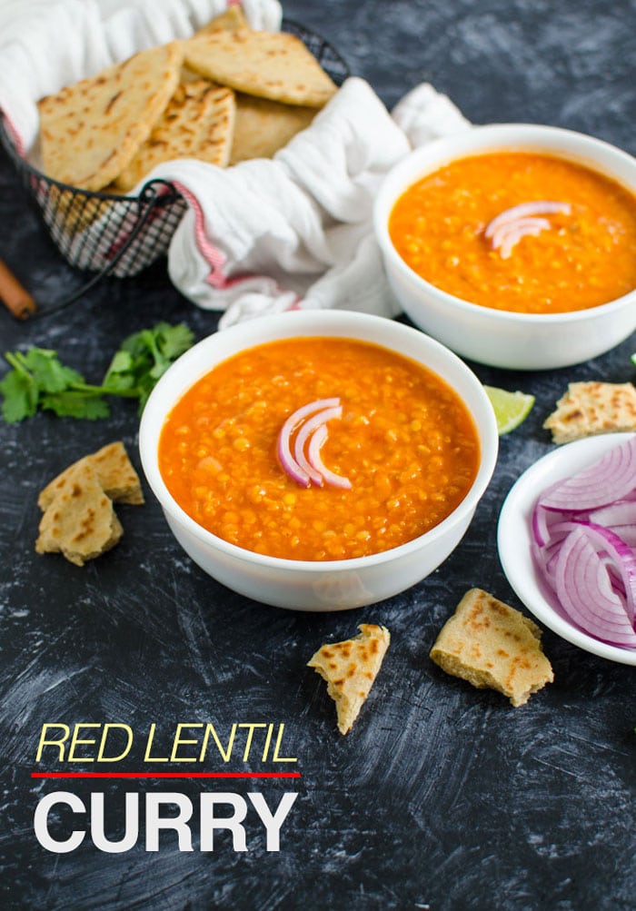 Side view of lentil curry in two serving bowl garnished with sliced onion and served with plain naan bread on the side. Image has text overlay 'Red Lentil Curry'