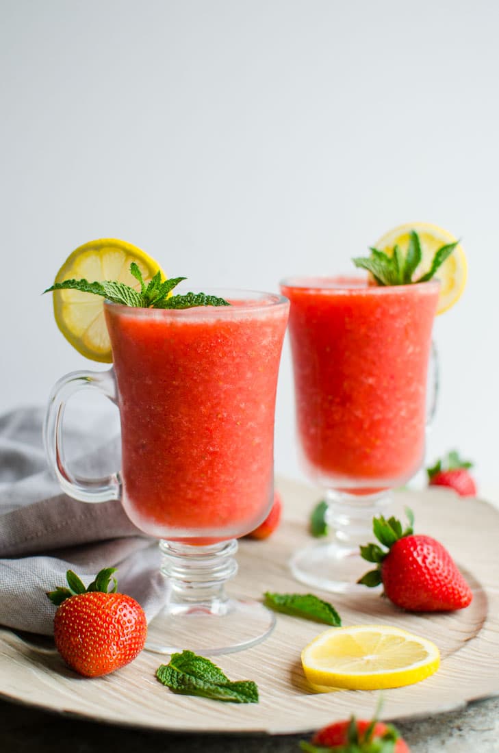Strawberry slush in serving glasses, garnished with lemon slice, and fresh mint leaves.