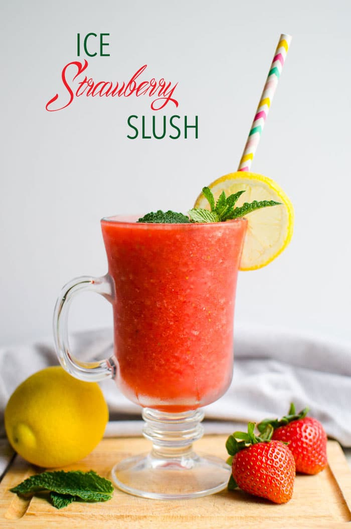 Strawberry slush in a serving glass with a paper straw, garnished with lemon slice, and fresh mint leaves.