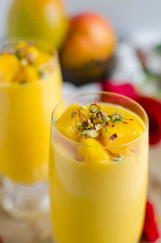 Healthy mango lassi in serving glasses, garnished with chopped pistachios and saffron threads.