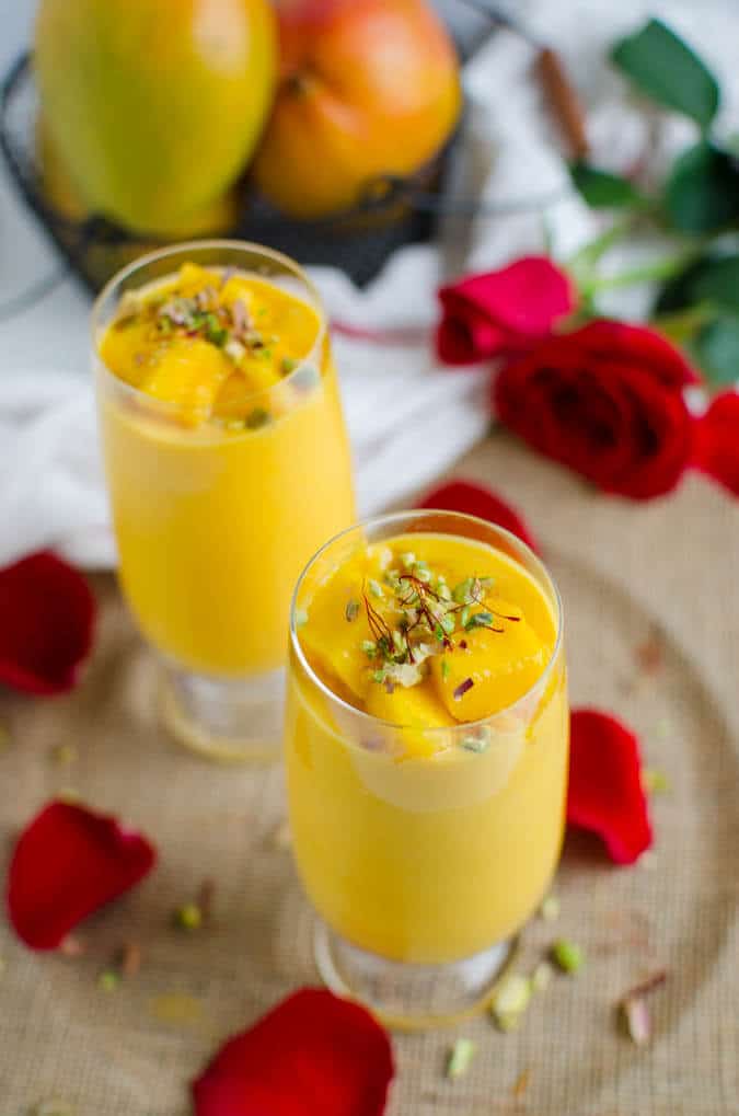 Healthy mango lassi in serving glasses, garnished with chopped pistachios and saffron threads.