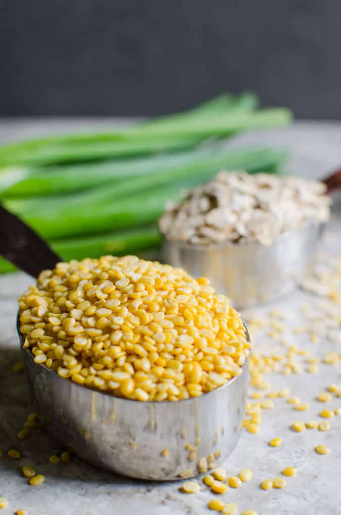 Raw mung beans, rolled oats and scallions on a flat surface.