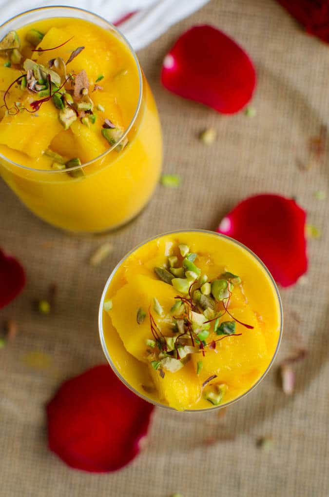 Healthy mango lassi in serving glasses, garnished with chopped pistachios and saffron threads.