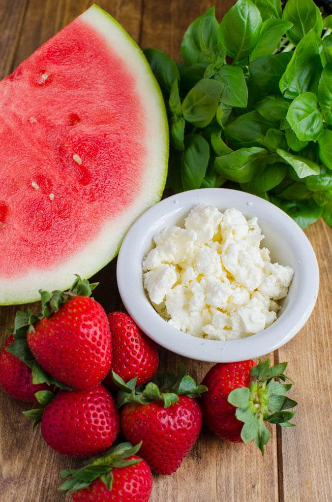 Watermelon, feta cheese, basil leaves and strawberry on a flat surface for making watermelon salad.