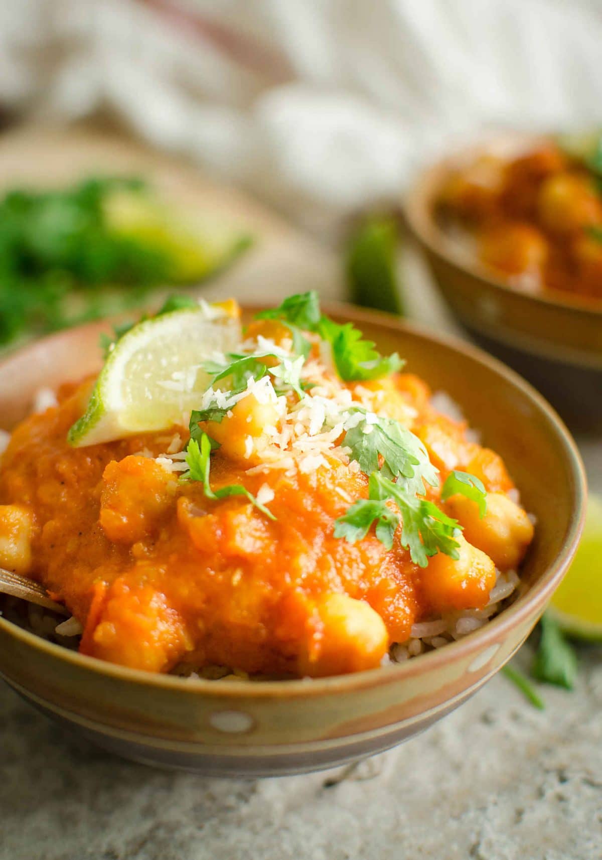 Coconut chickpea curry garnished with fresh cilantro and lime wedges in a serving bowls.