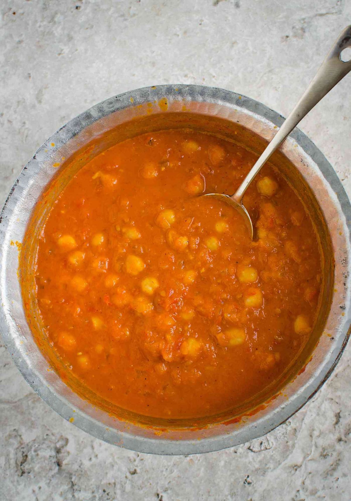 Cooked chickpea curry with coconut in a metal pot with a metal serving spoon.