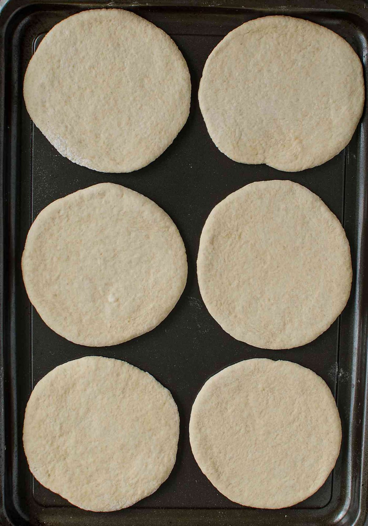 Whole wheat dough rolled into flatbreads and placed them in a baking tray.  
