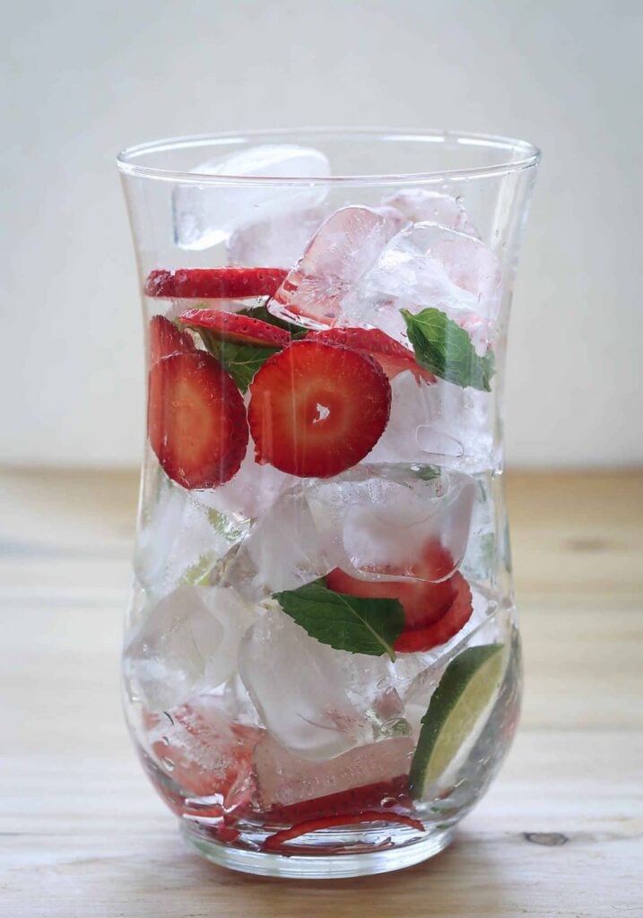 Strawberry slices, mint leaves, lime slices and ice in large glass jar.