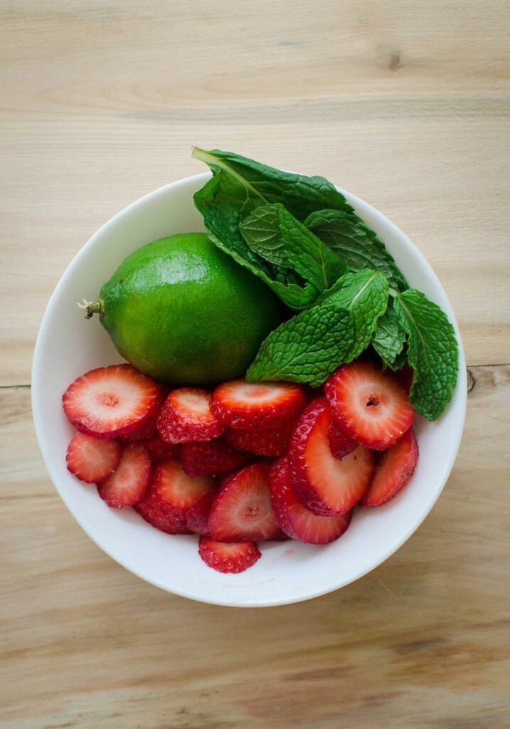 Strawberry slices, mint leaves and lime in a ceramic bowl.
