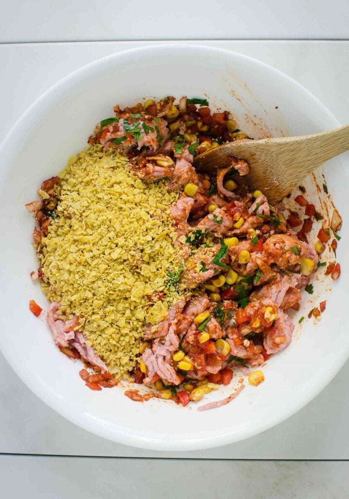 Ground turkey with crushed tortilla chips, veggies and spices in a mixing bowl with wooden spatula.