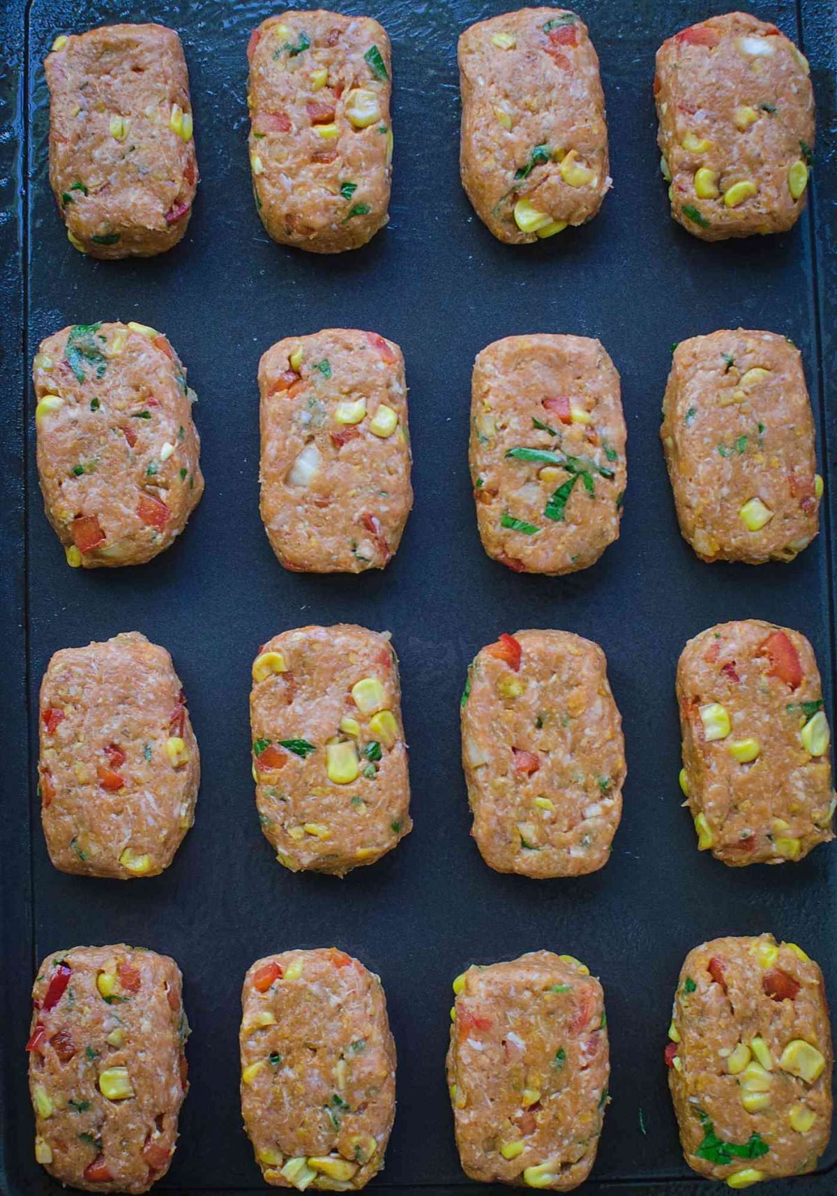 Prepared raw mini turkey meatloaves on a tray and are ready to grill.