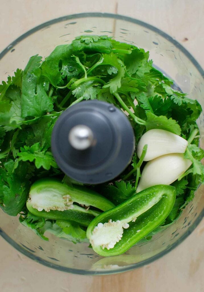 Fresh cilantro, jalapeño and garlic in food processor jar.
