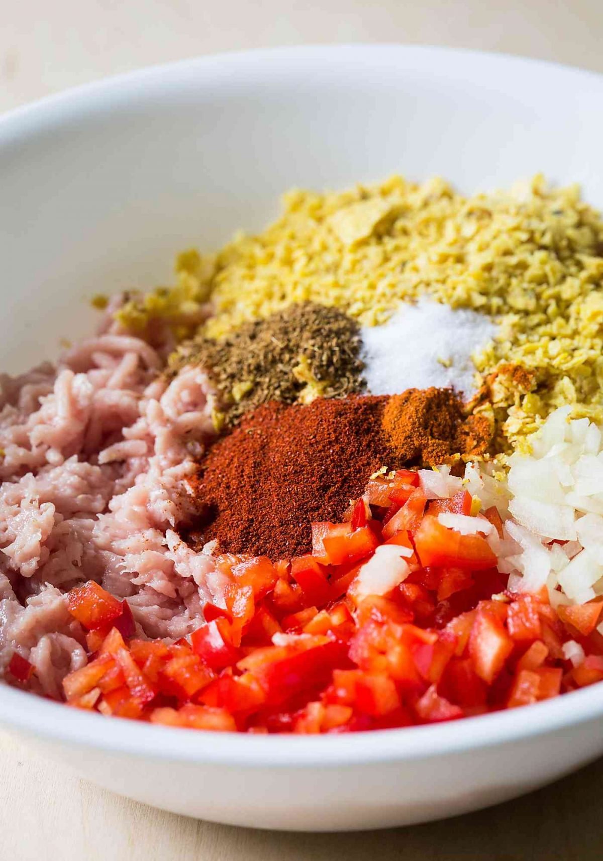 Ground chicken with diced pepper, onion and spices in a mixing bowl. 