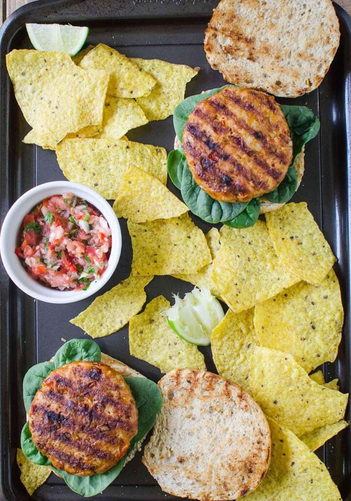 grilled ground chicken patties with burger buns, tortilla chips and salsa ready to assemble into a burger.