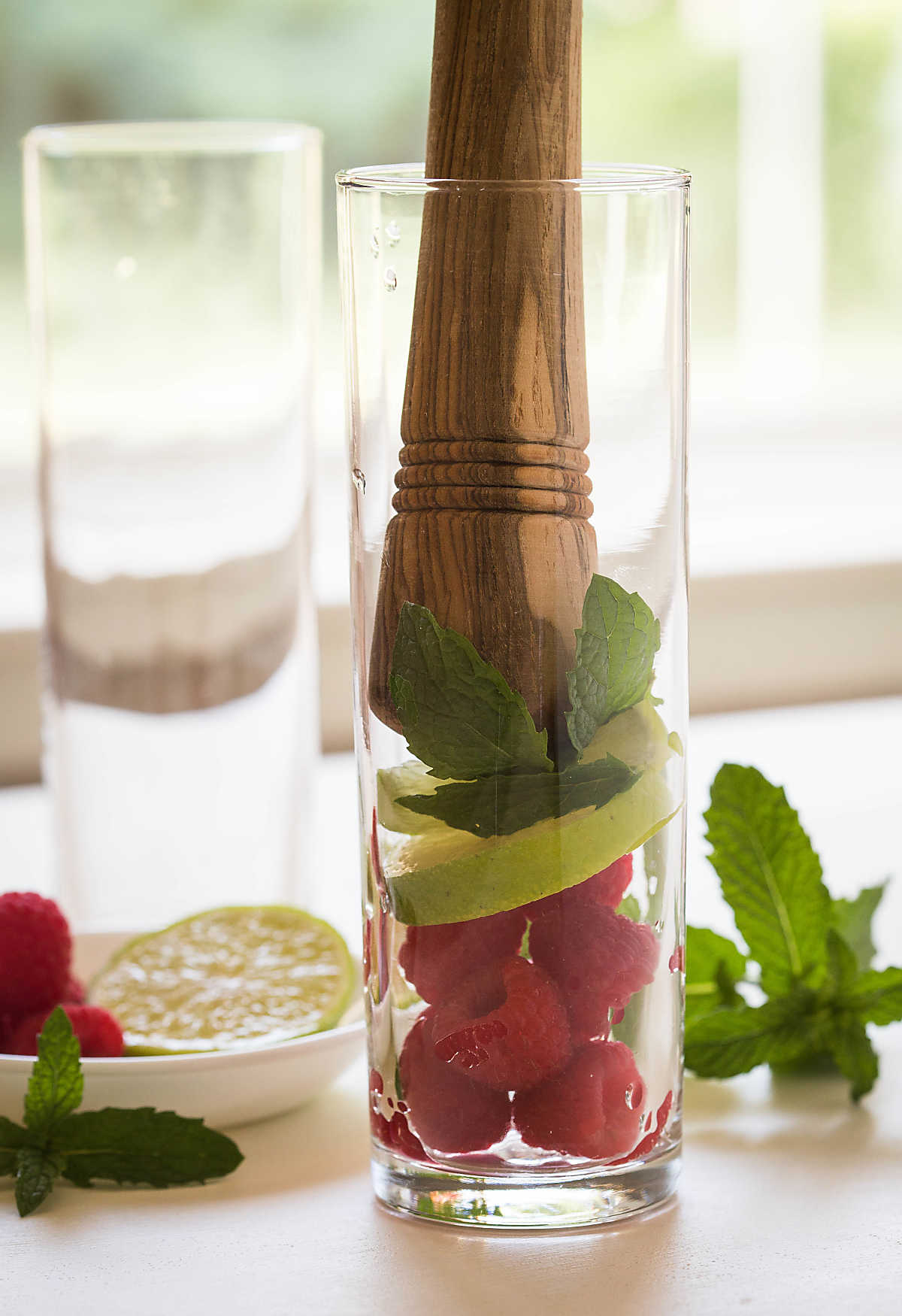 Fresh raspberries with lime slices and mint leaves in a glass with wooden muddler.
