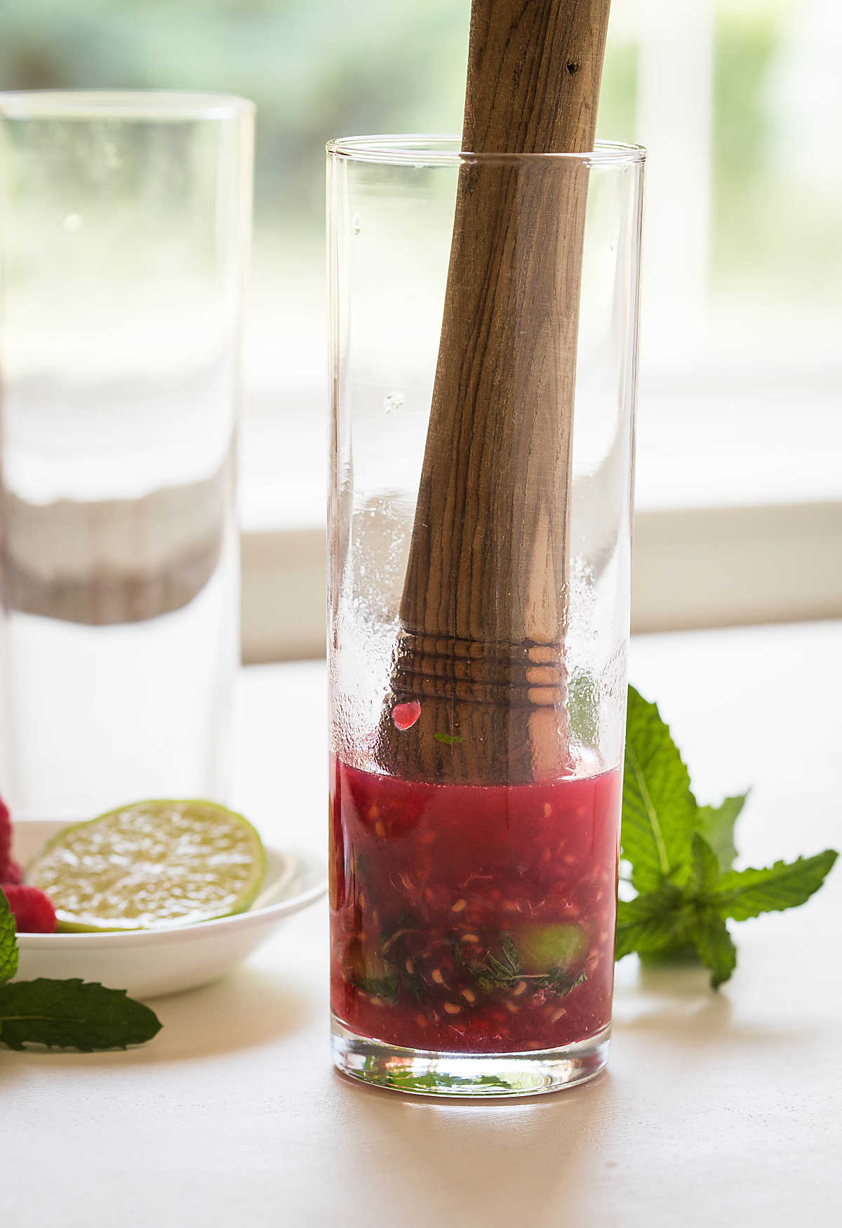 Smashed fresh raspberries with lime slices and mint leaves in a glass with wooden muddler.