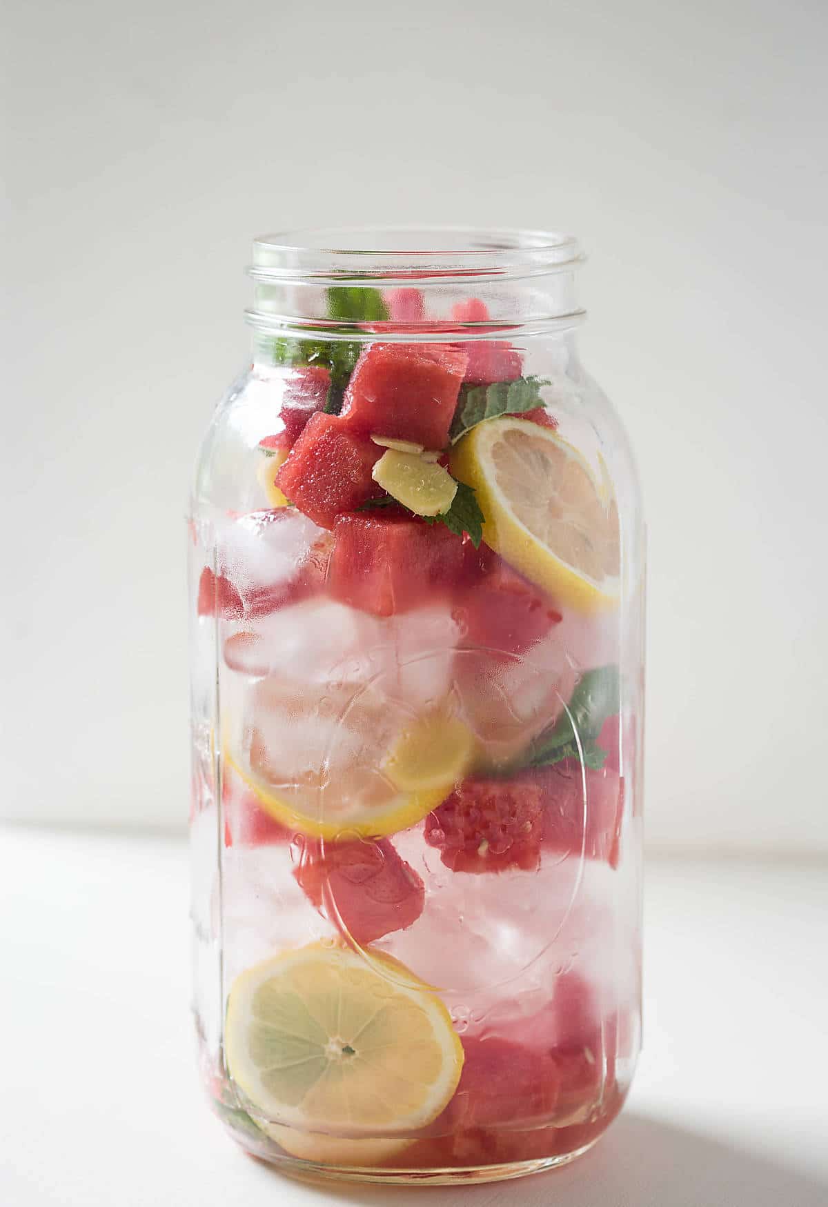 Watermelon cubes, lemon slices, ginger, mint and ice in a mason jar for making summer cooling water. 