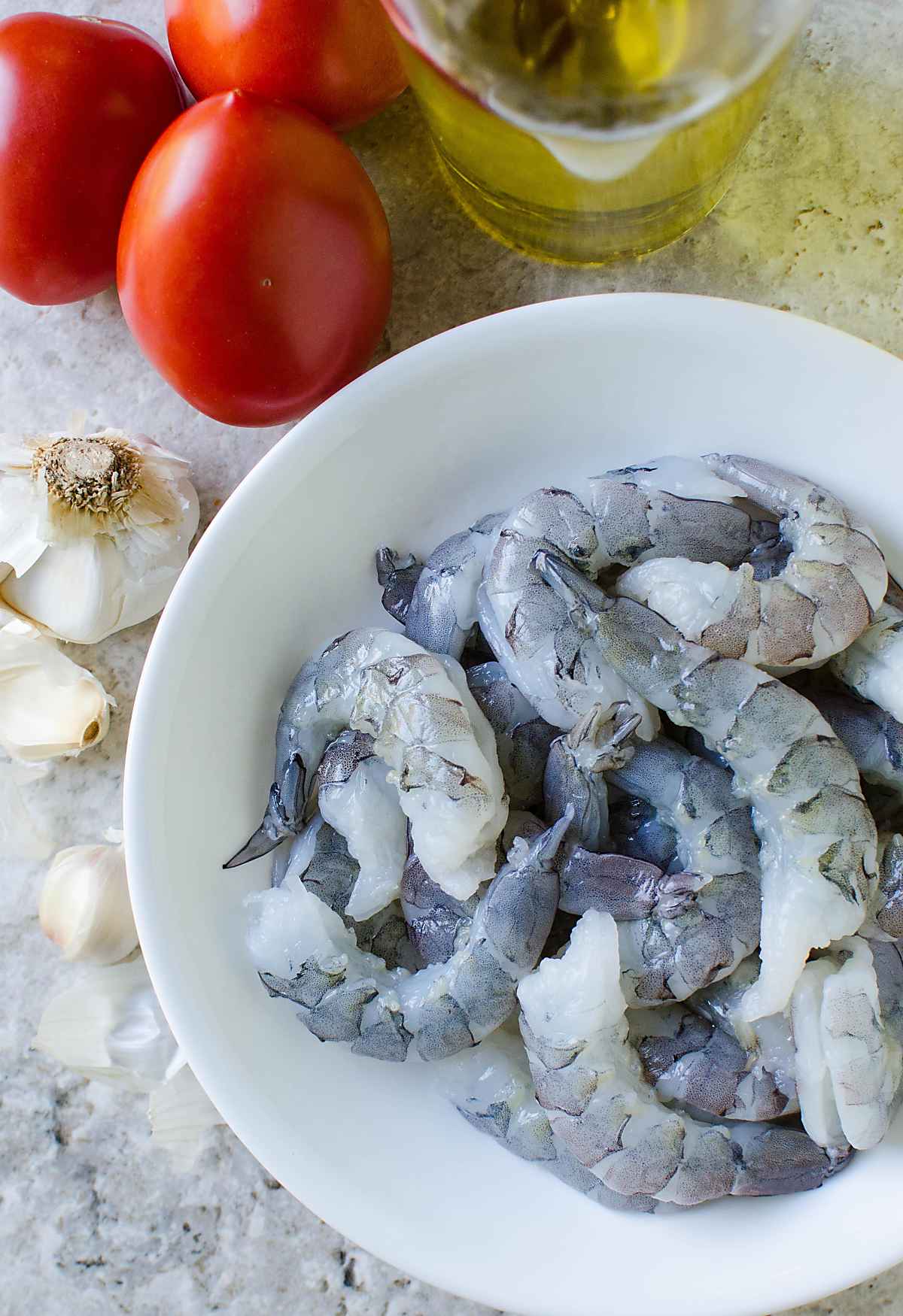 Cleaned and deveined shrimp in a ceramic bowl, fresh tomato, garlic and oil for making shrimp in tomato sauce.