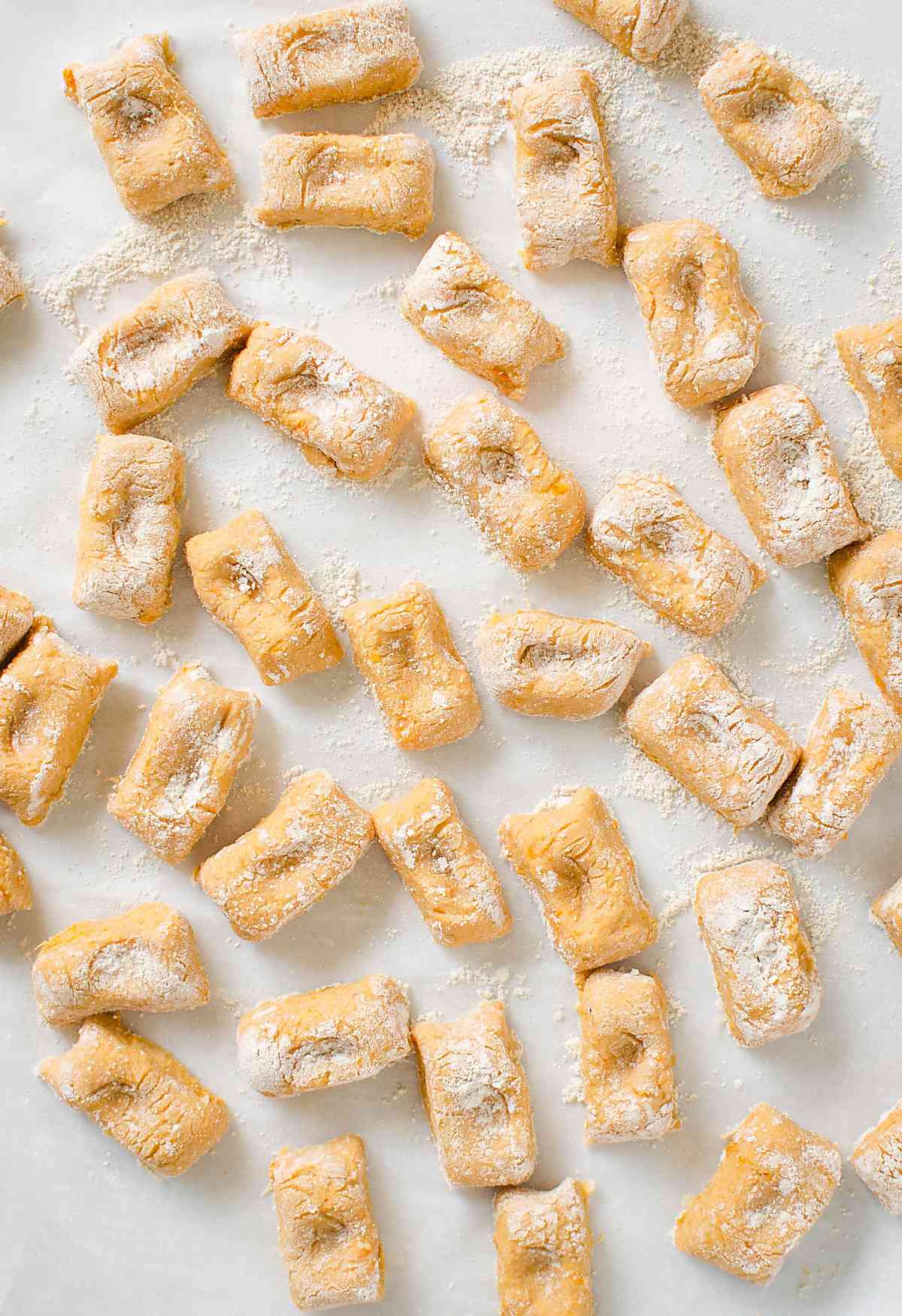 Homemade raw sweet potato gnocchi dusted with dry flour and spread over the flat surface.