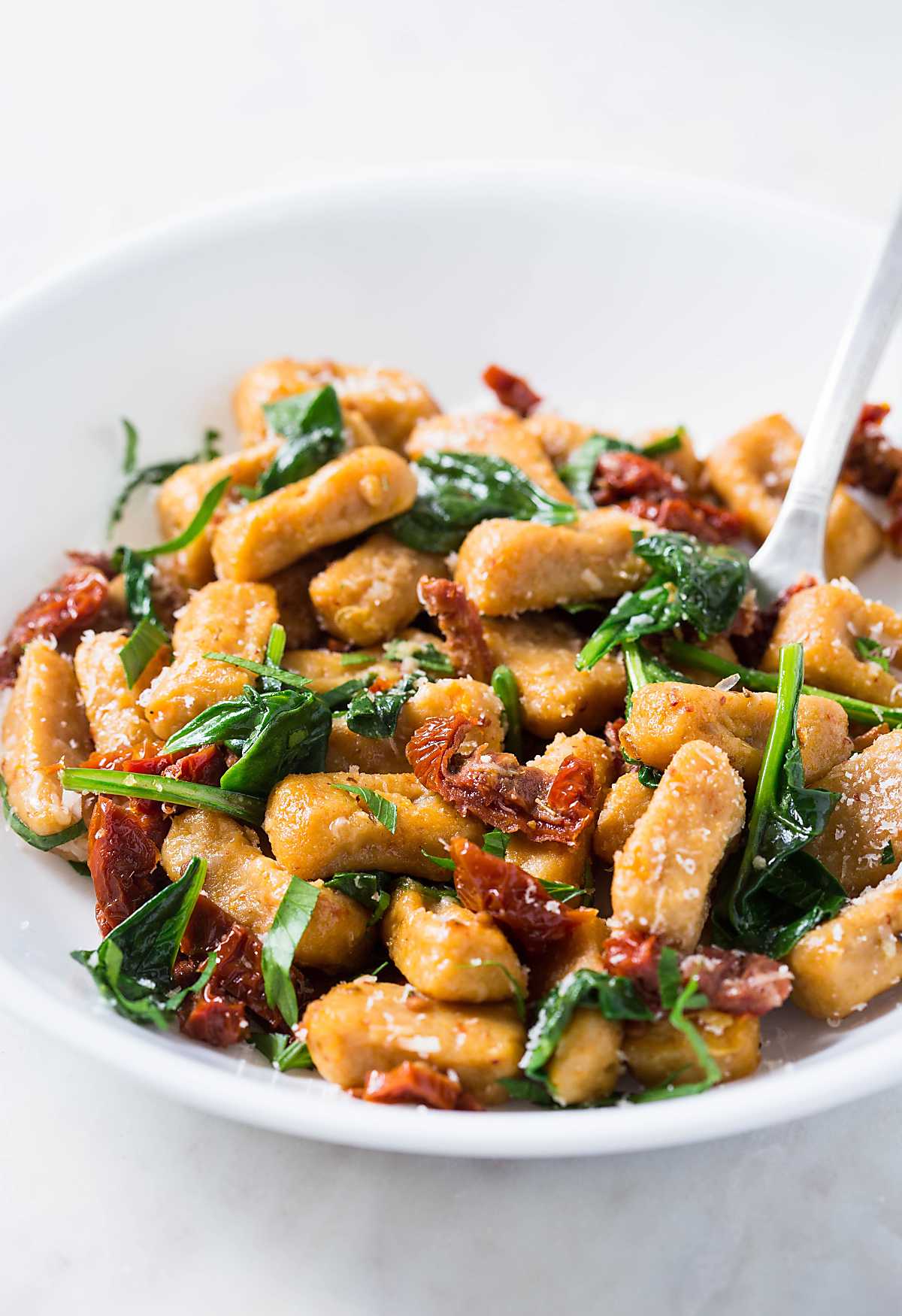 Sweet potato gnocchi with spinach and sundried tomato in a serving bowl.