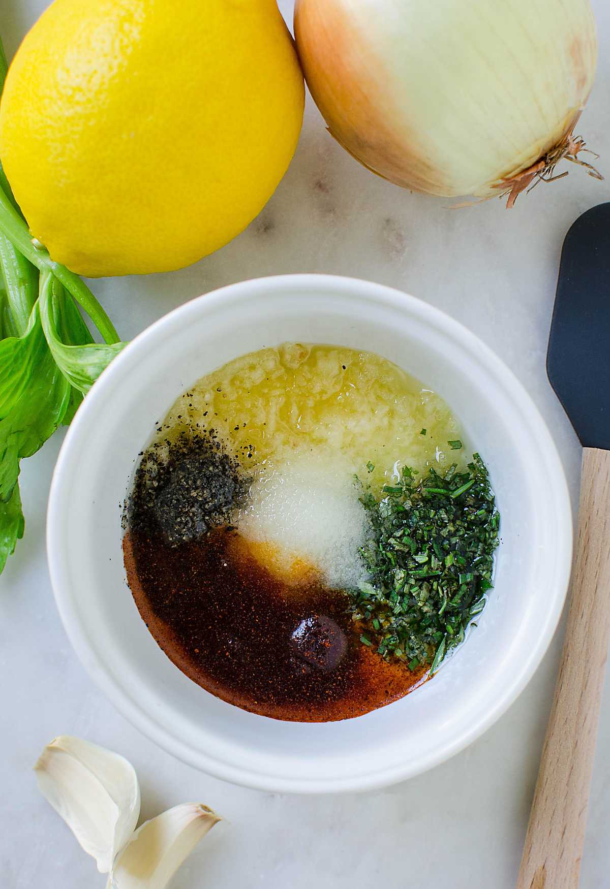 Dry herbs, salt, garlic and paprika with oil in small mixing bowl and fresh lemon and onion on the side.