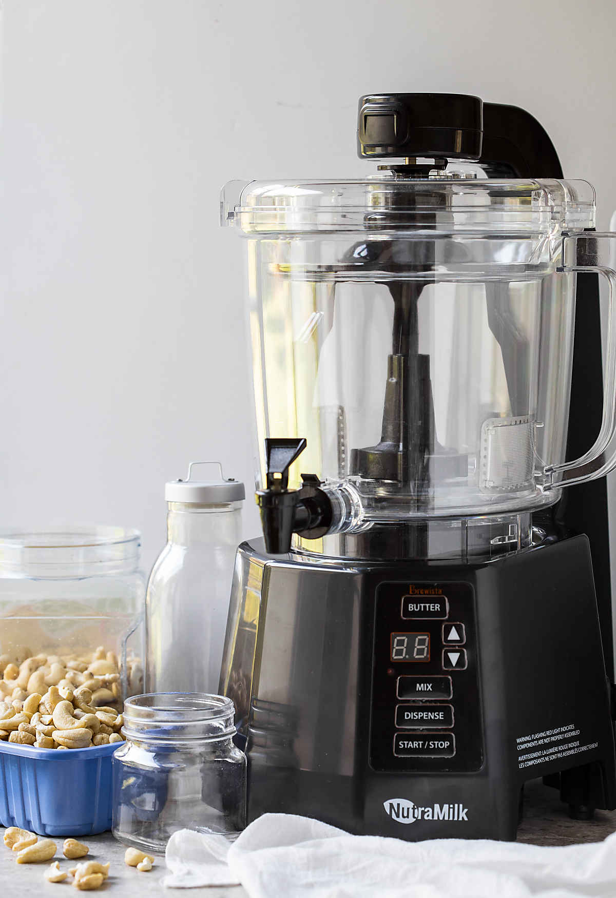 The Nutramilk machine with empty glass bottle, glass bowl and raw cashews.