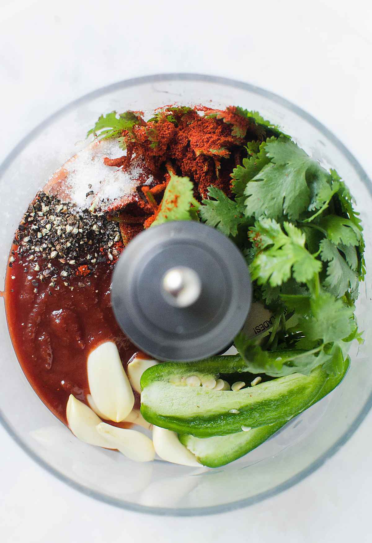 Garlic, jalapeño, cilantro and spices in a food processor jar. 