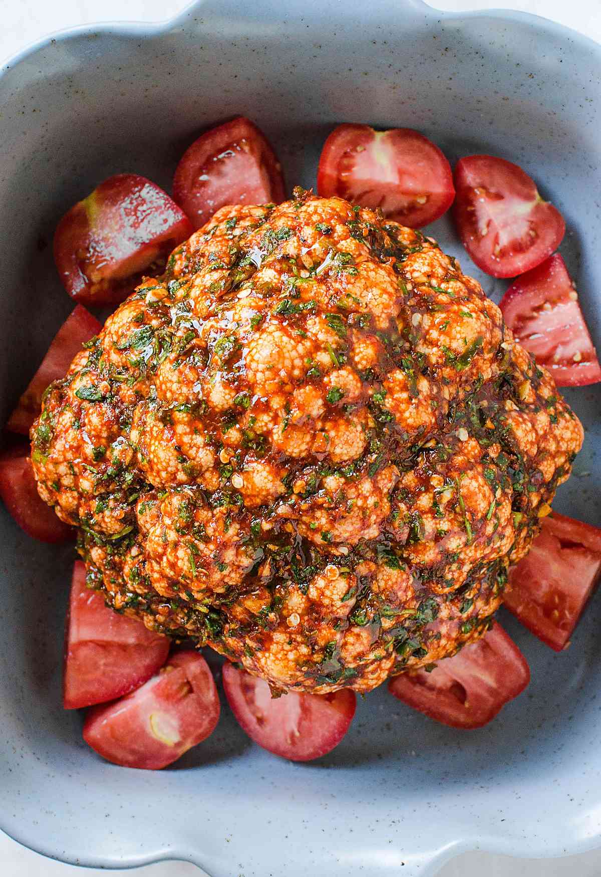 Whole cauliflower with tomatoes and herbs in baking dish and is ready to bake.