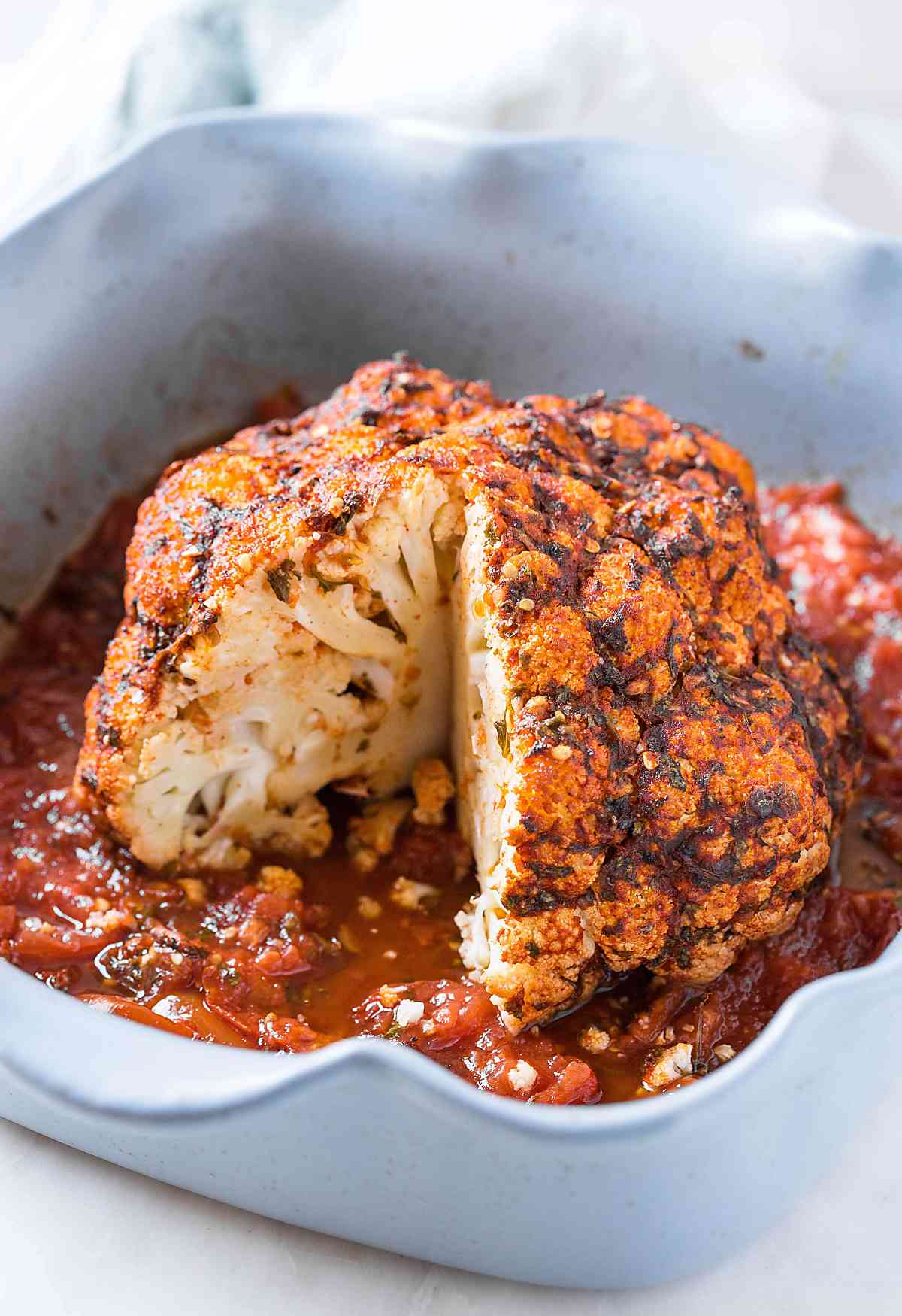 Whole roasted cauliflower with tomato and herbs in baking dish.