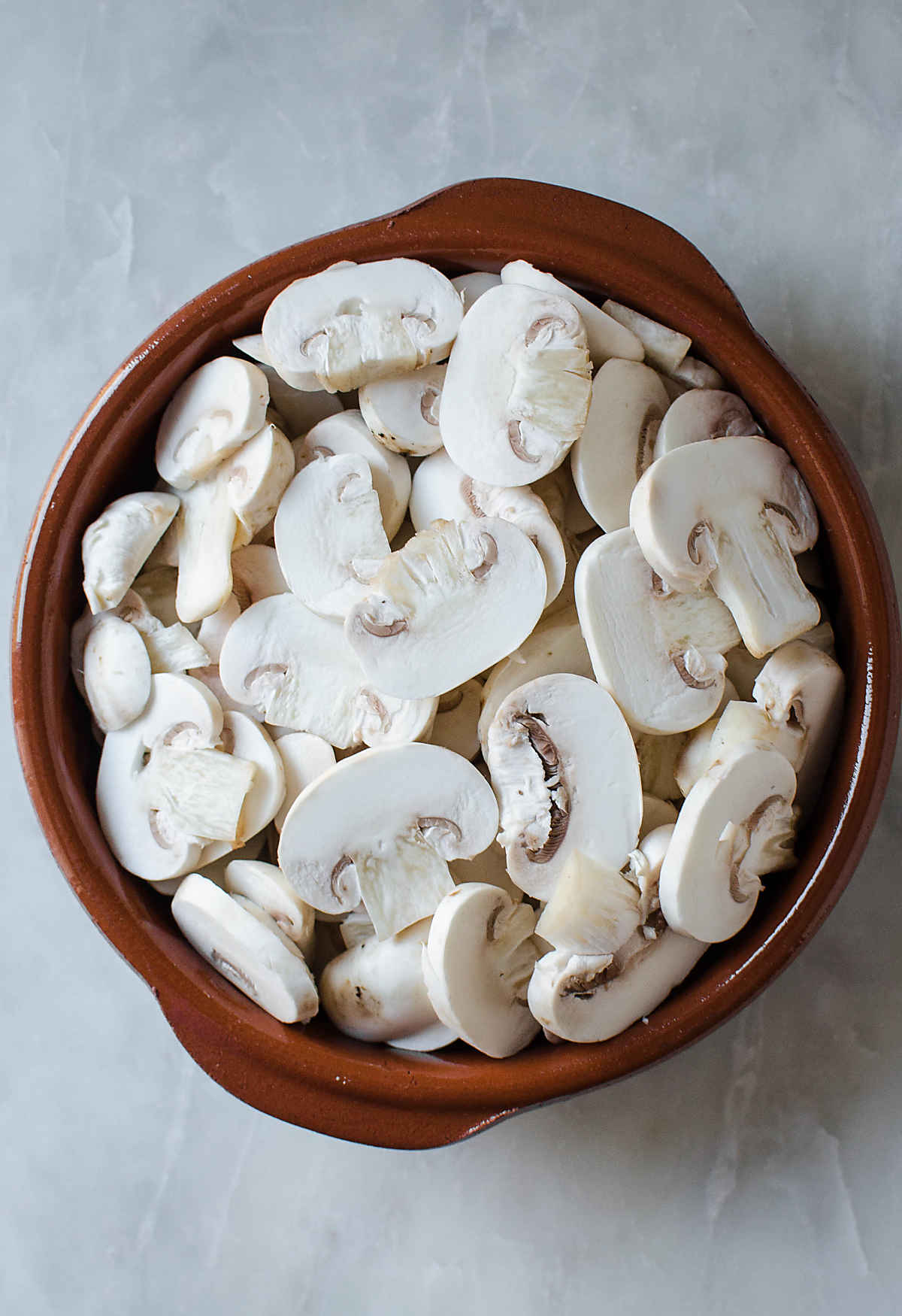 Sliced white button mushrooms fin a flat dish.