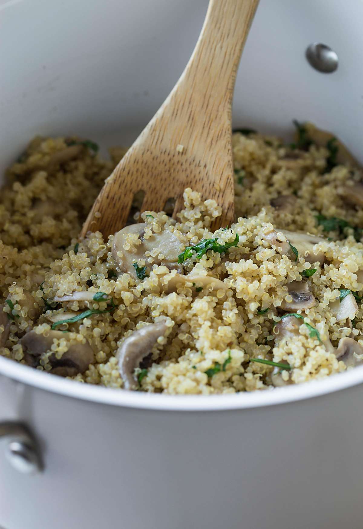 Stirring healthy mushroom and quinoa in a pot with wooden spatula.