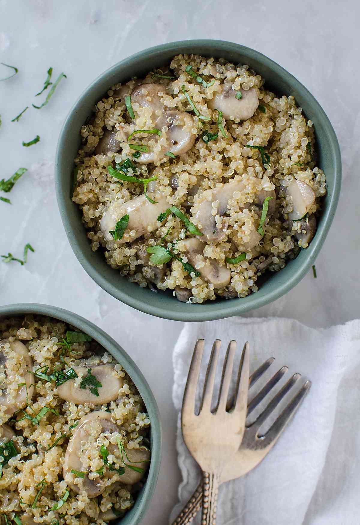 healthy garlic mushroom quinoa served in a serving bowls with metal forks on the side.