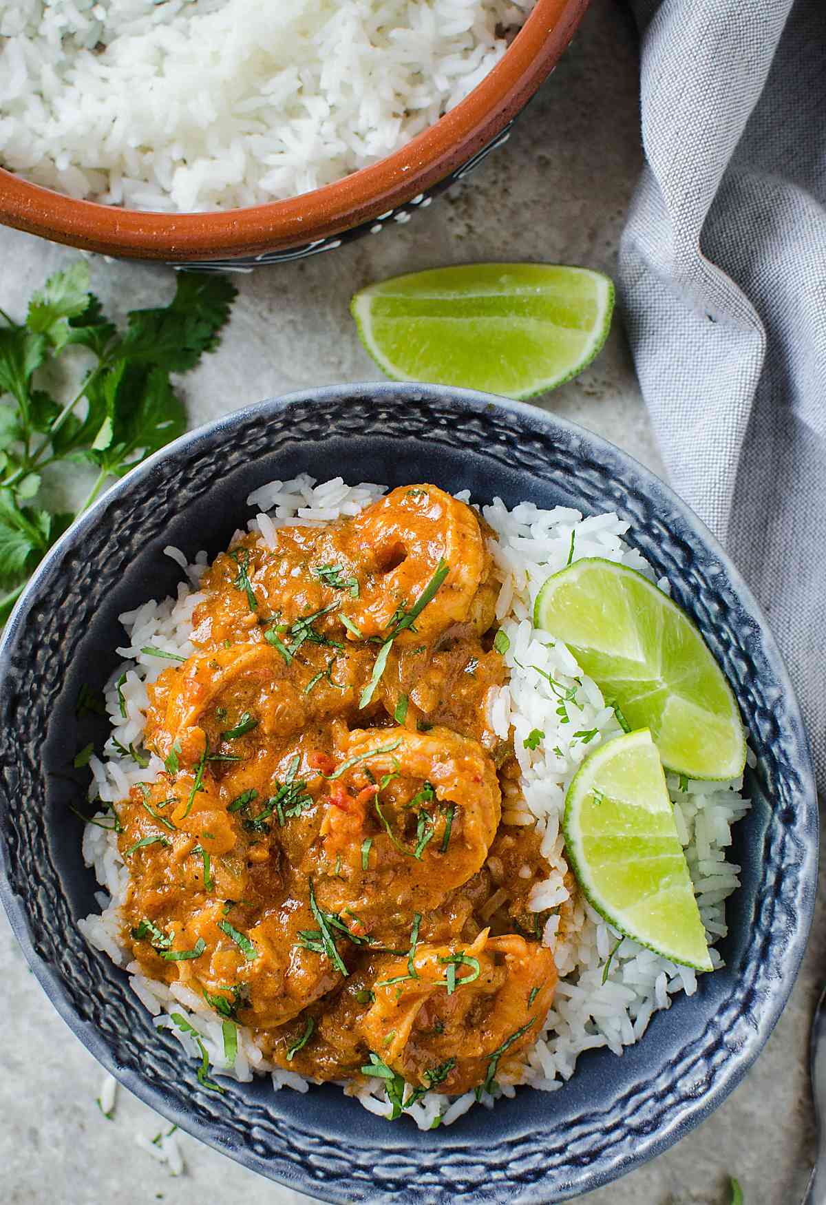 shrimp curry with served over rice  and lime wedges on the side in a serving bowl.