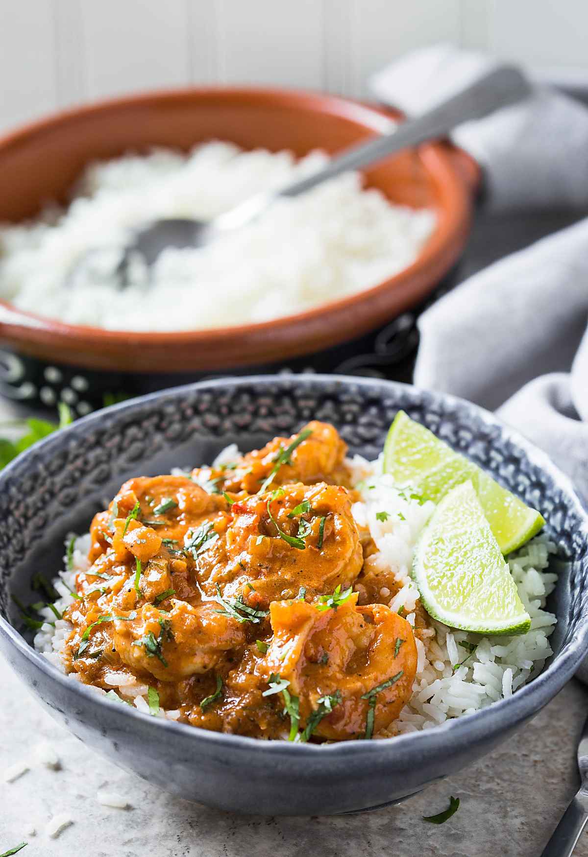 Coconut shrimp curry served over rice and lime wedges on the side in a serving bowl.