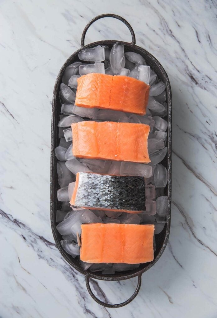 raw salmon fillets are spread over ice cubes in a tray