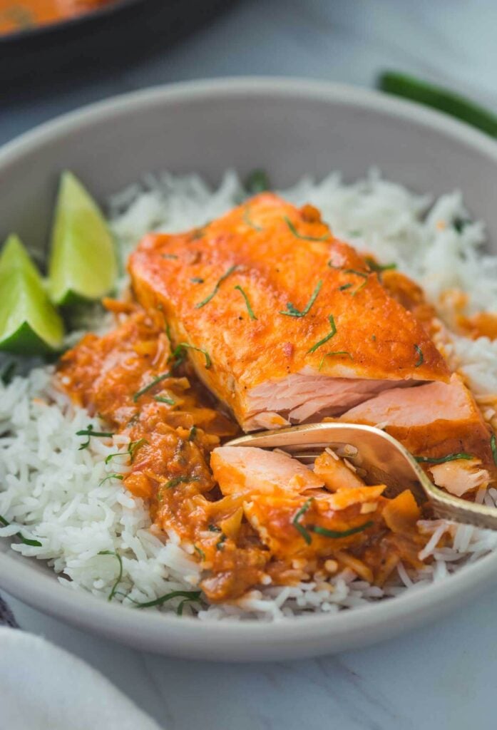 Indian salmon curry with coconut served in a deep plate with white rice and lemon wedges on the side.