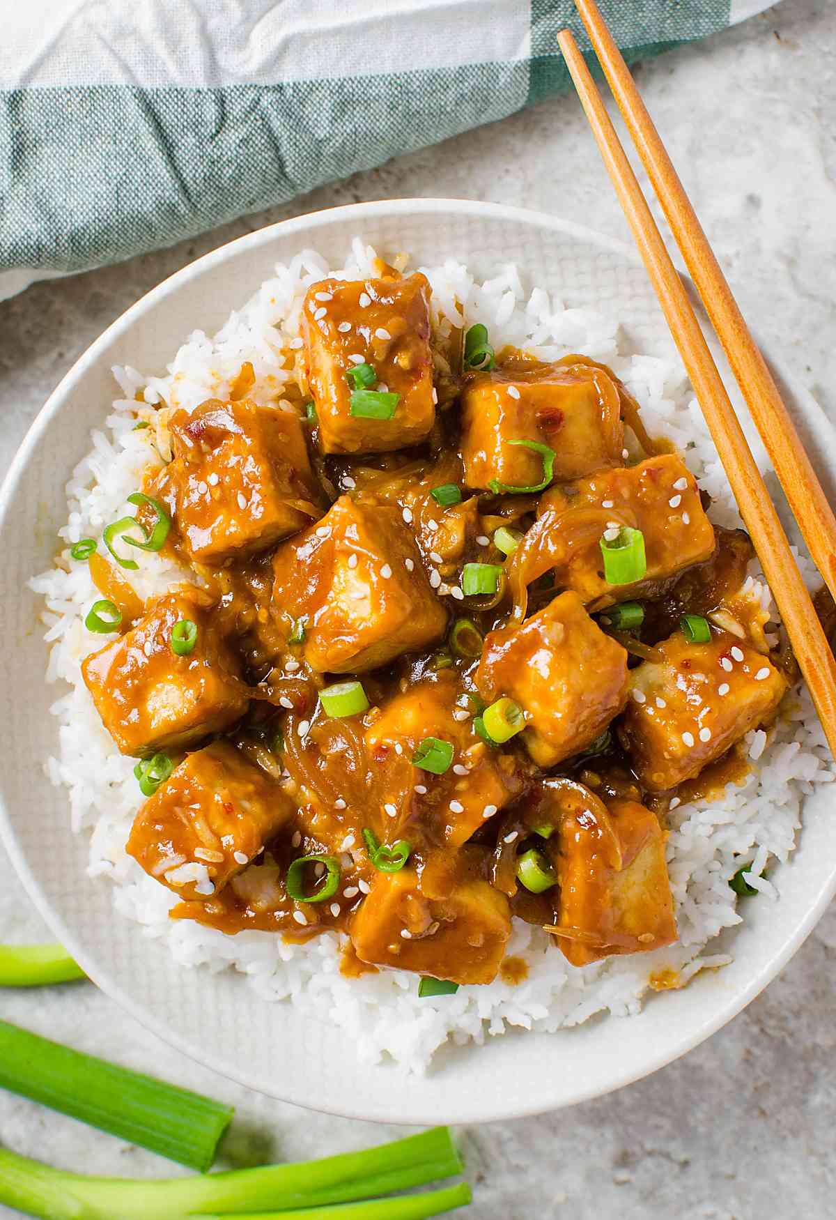 Tofu with chili garlic sauce served over bed of steamed rice in a serving bowl with wooden chopsticks.