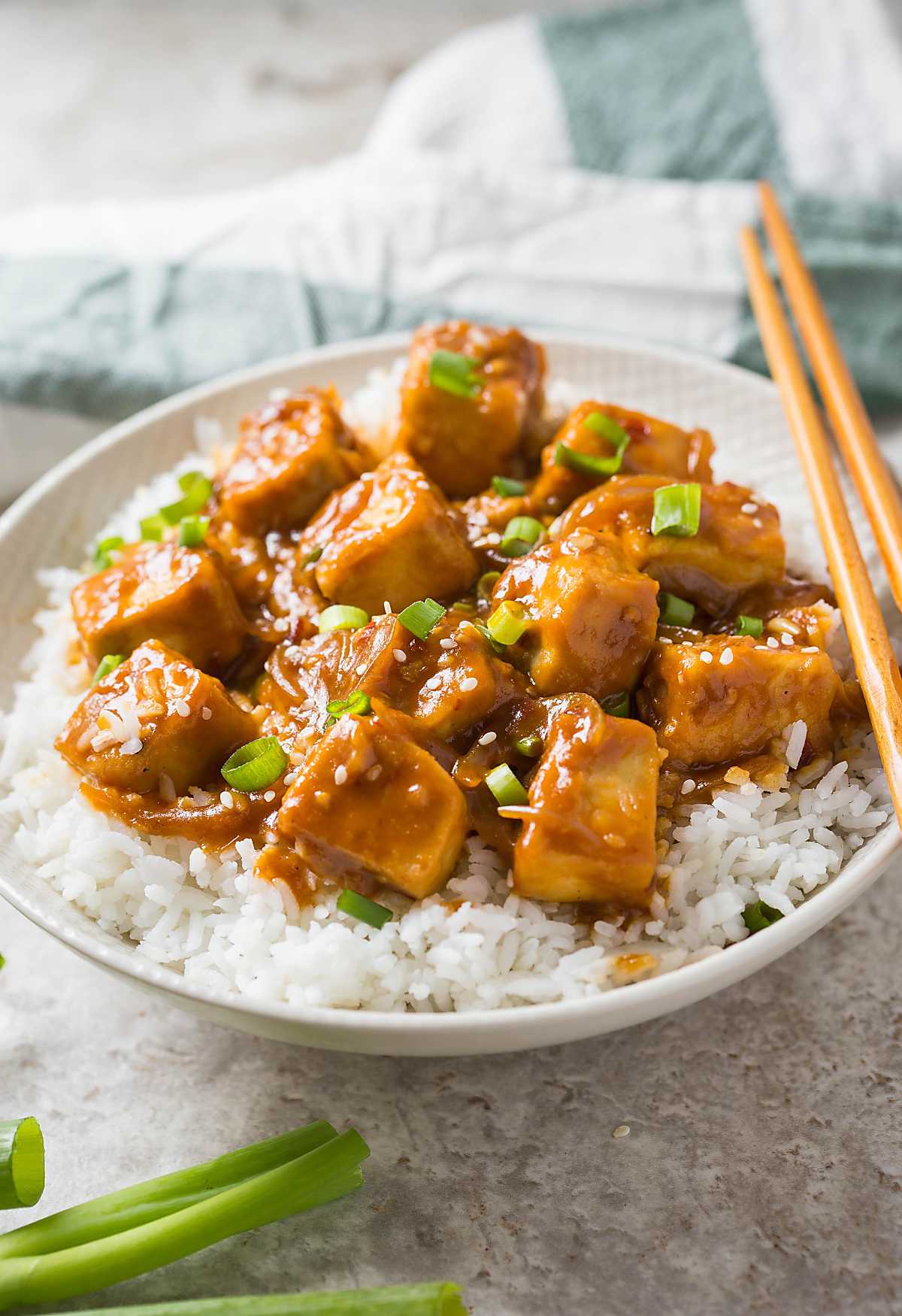 Tofu with chili garlic sauce served over bed of steamed rice in a serving bowl with wooden chopsticks.