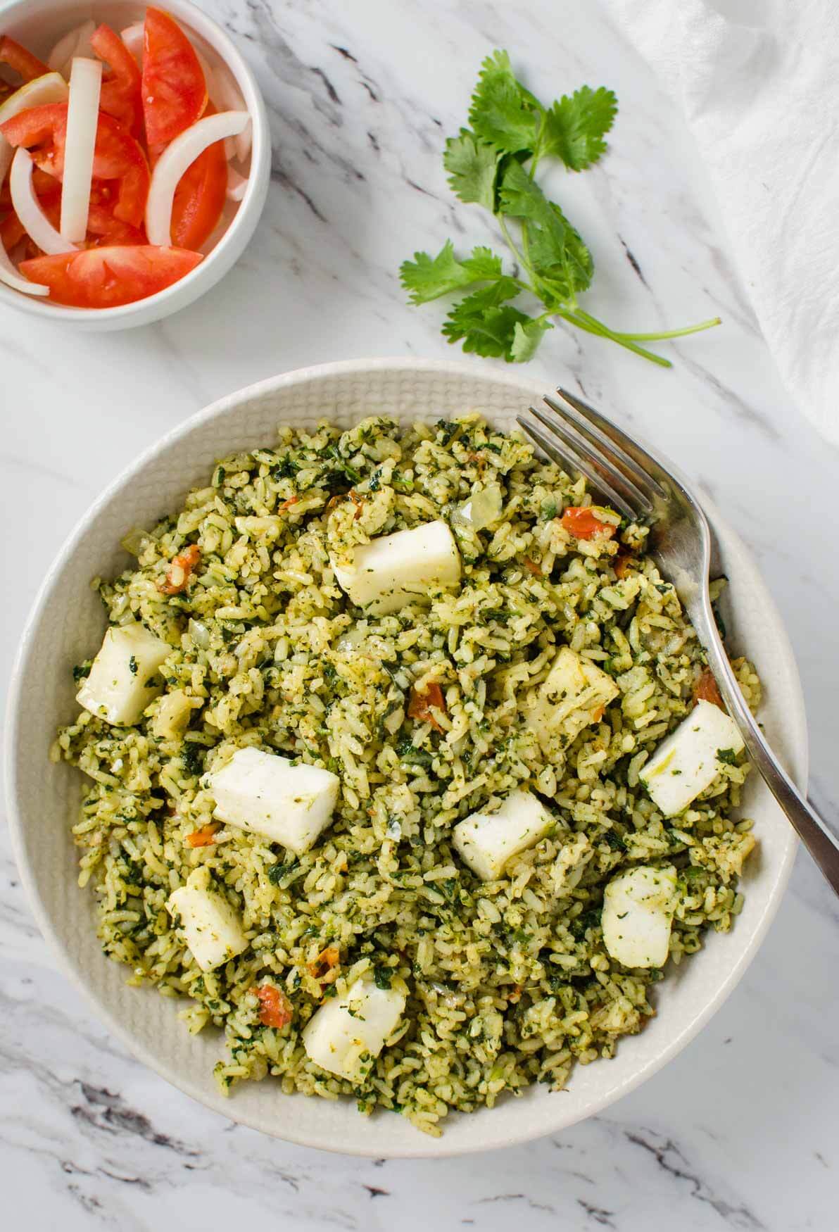 Palak paneer rice in a bowl with a metal fork. 