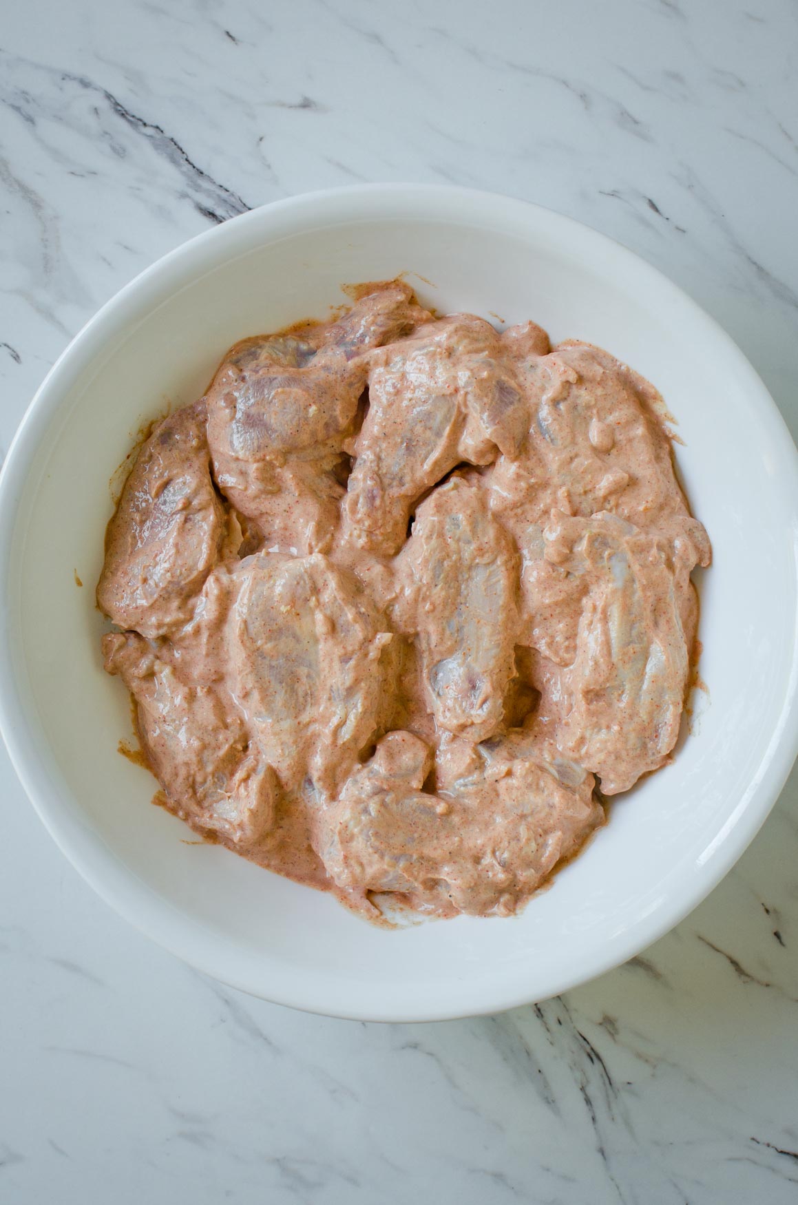 Chicken wings marinated in yogurt and Indian spices in a large bowl for making tandoori chicken wings.