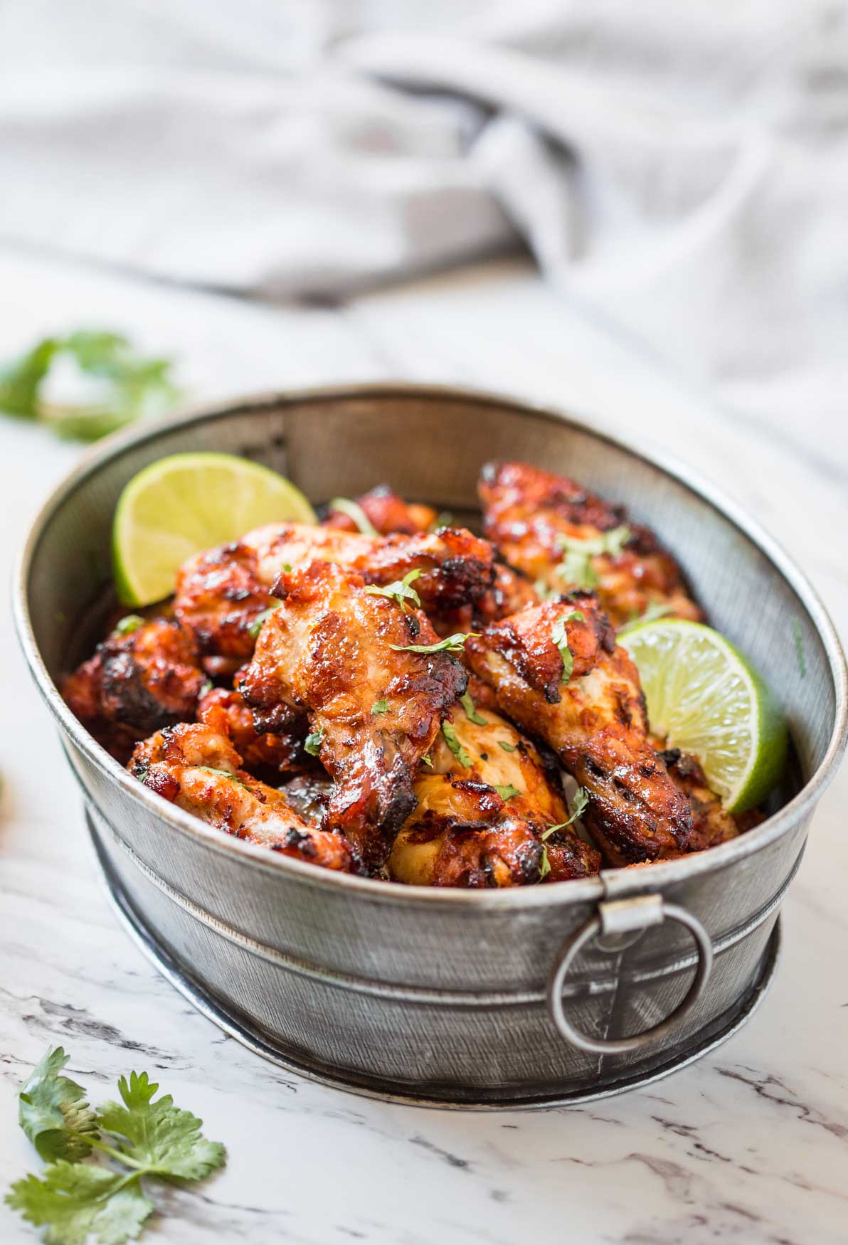 Grilled tandoori chicken wings in metal serving container. Garnished with lime wedges and fresh cilantro. 