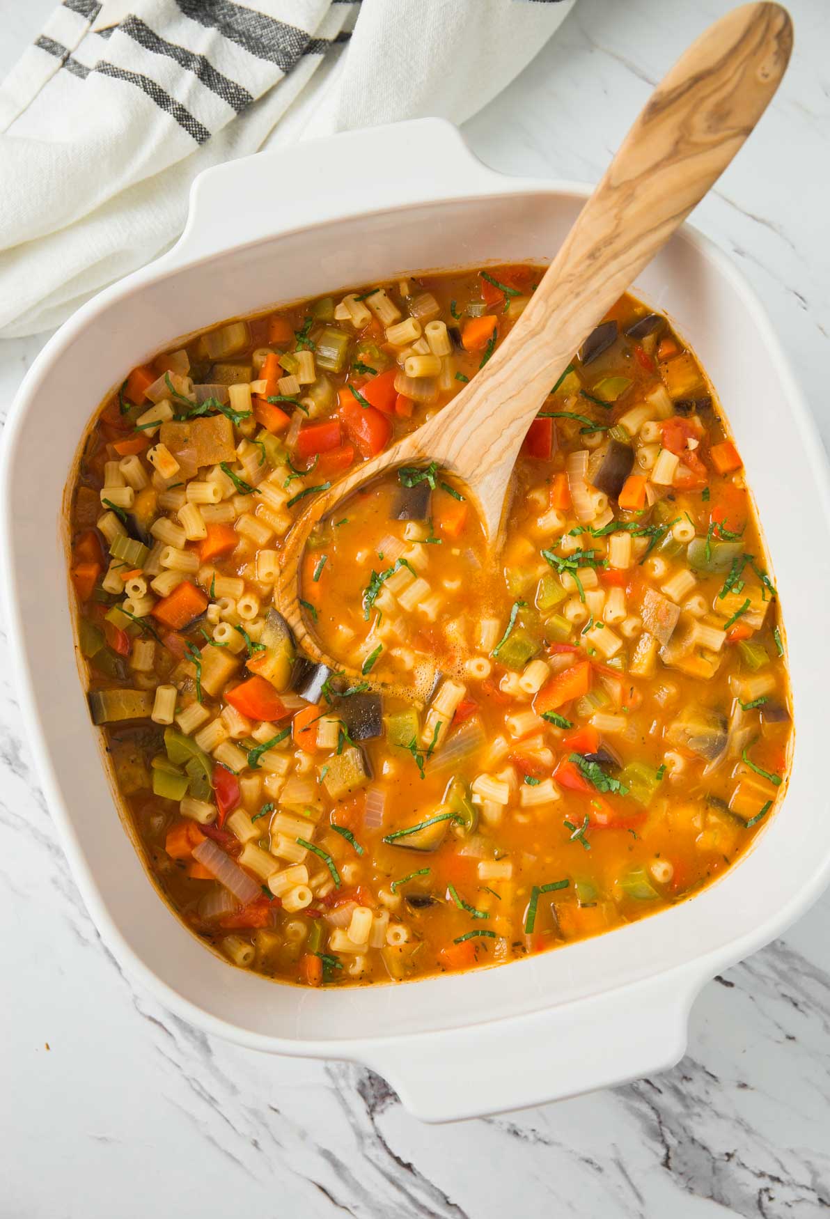 Vegetable pasta soup in a ceramic pot with wooden ladle.