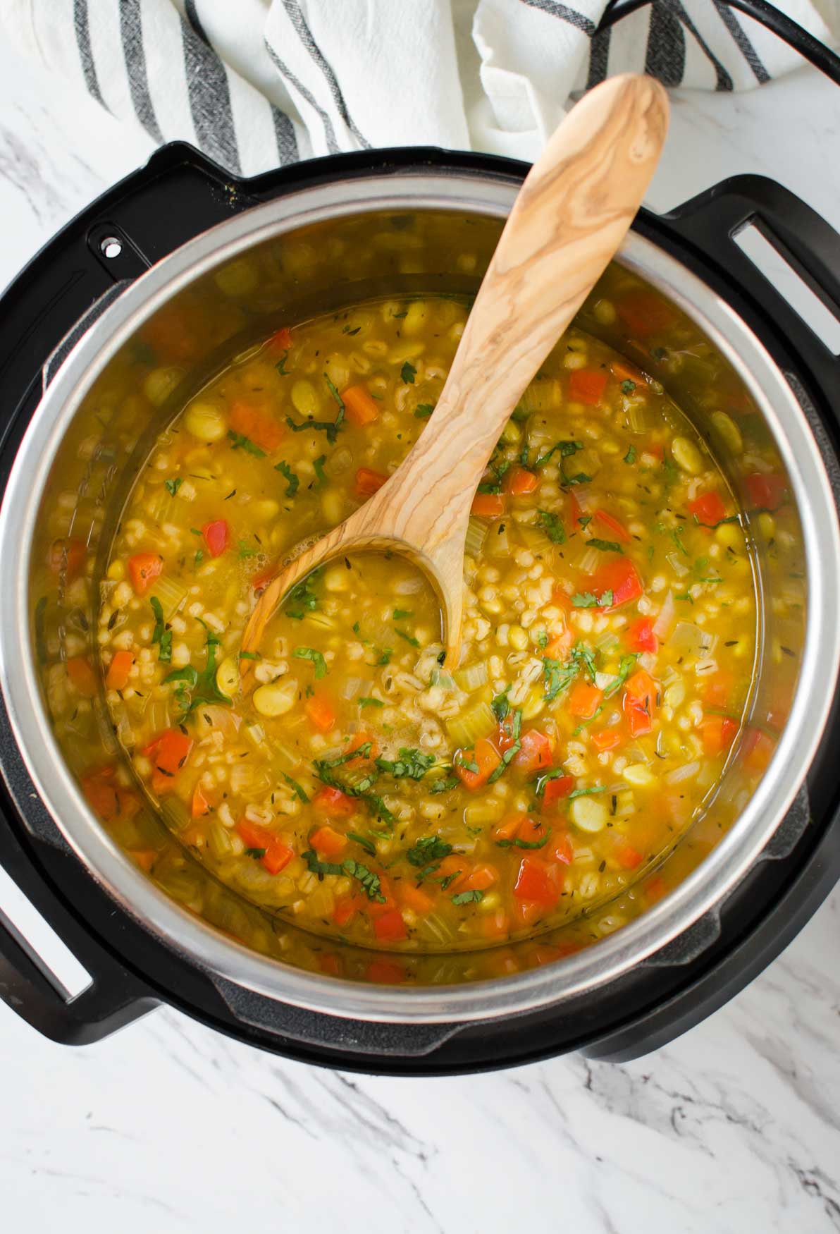 Vegetable barley soup in Instant Pot with wooden ladle.