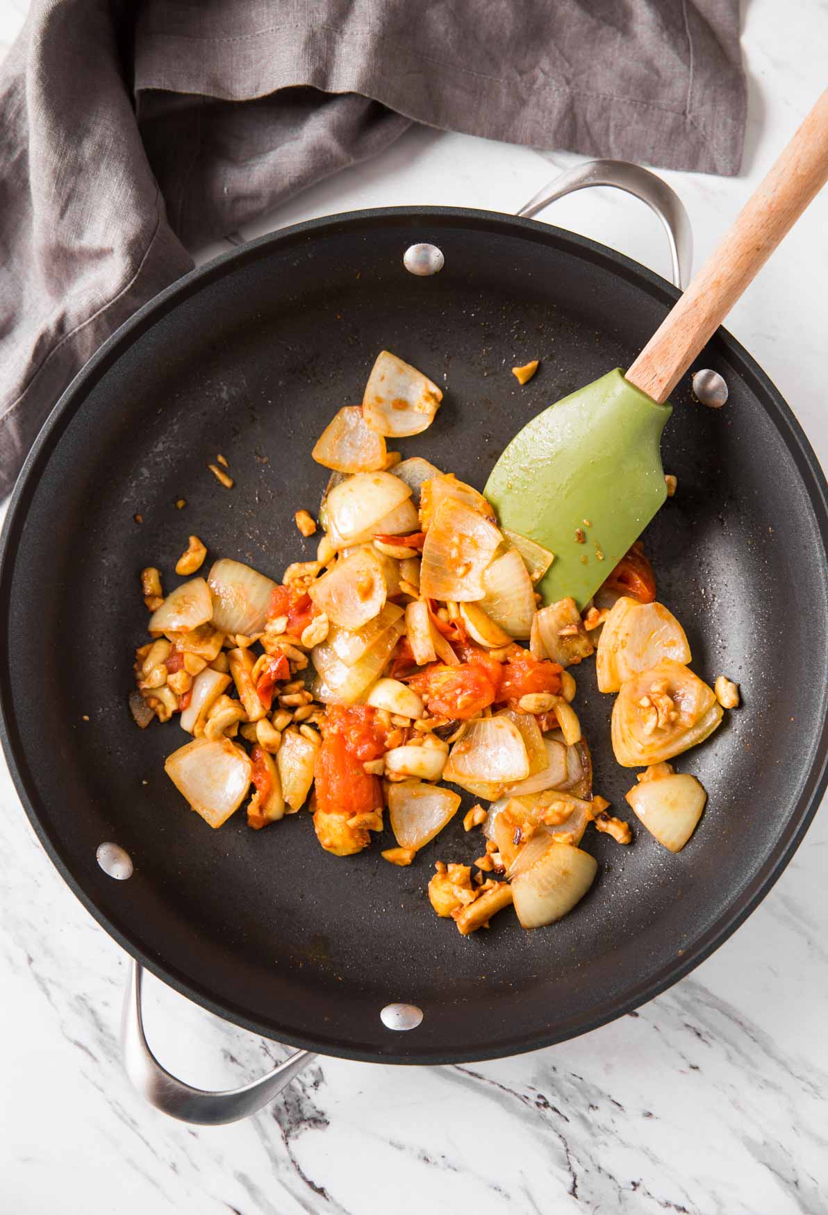 Cooking onion and tomato mixture in a nonstick skillet for making the base for green spinach curry.