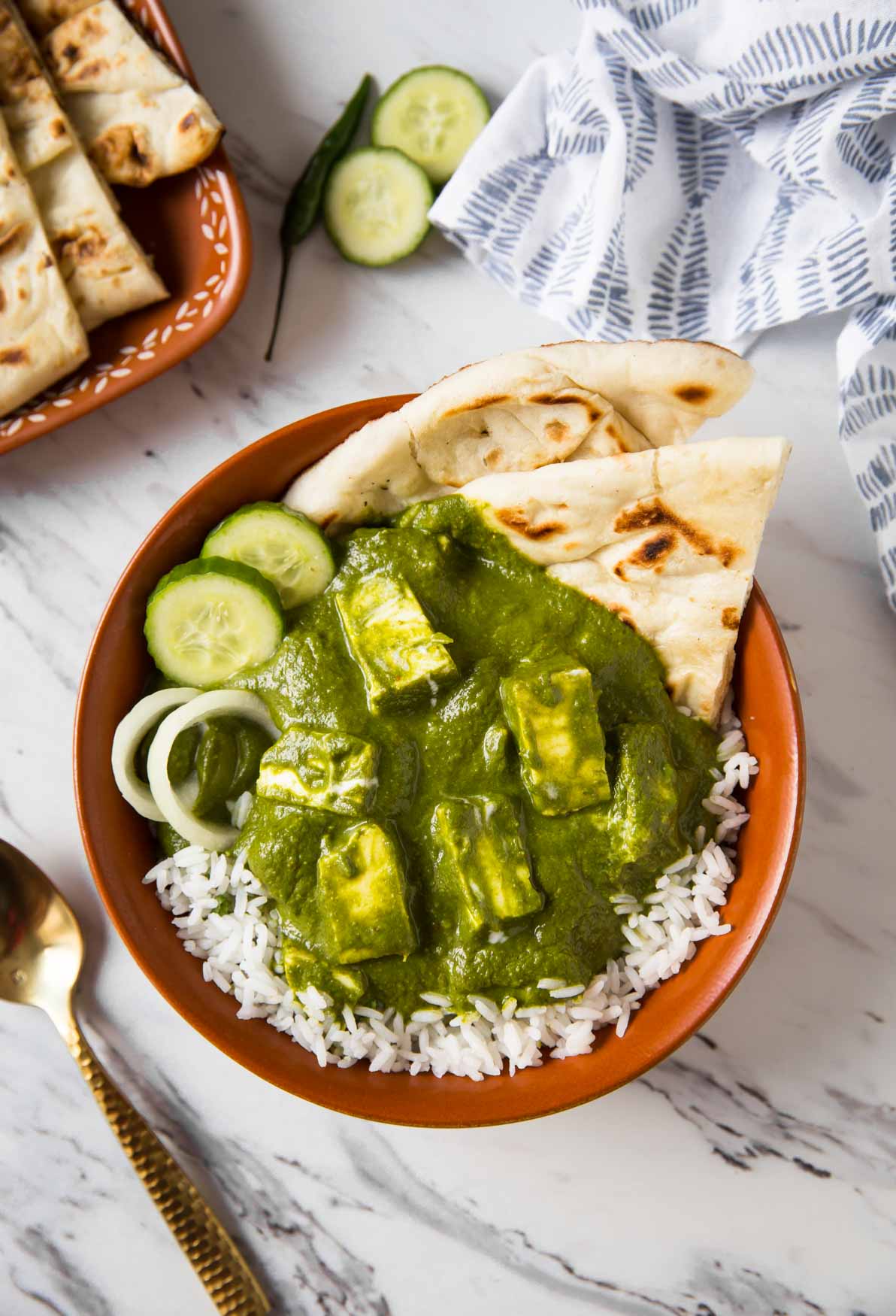 Palak paneer curry over a bed of rice with naan bread in a serving dish.