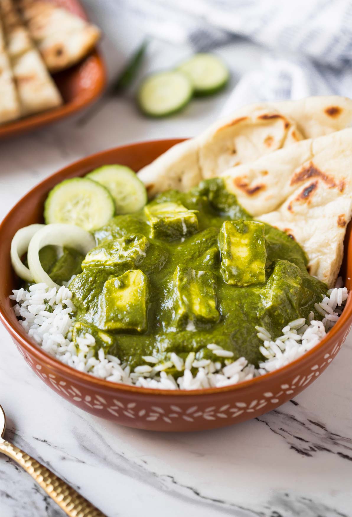 Palak paneer curry over a bed of rice with naan bread in a serving dish.